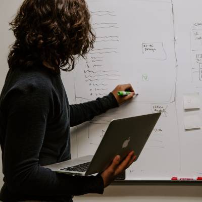person holding a laptop while writing on a whiteboard